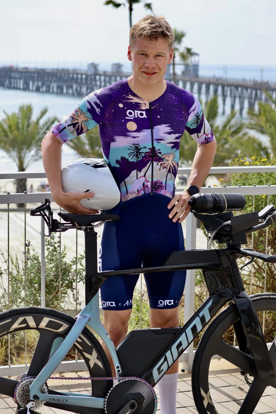 Sigurd Elvestad smiling by the sea, holding his helmet next to his time-trial bike